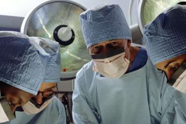 Four surgeons in scrubs and masks focused on a surgical procedure.