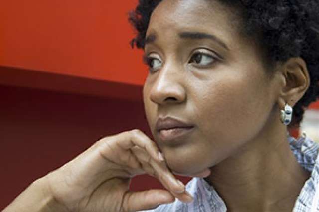 African American woman thoughtfully resting her chin on her hand against a red backdrop.