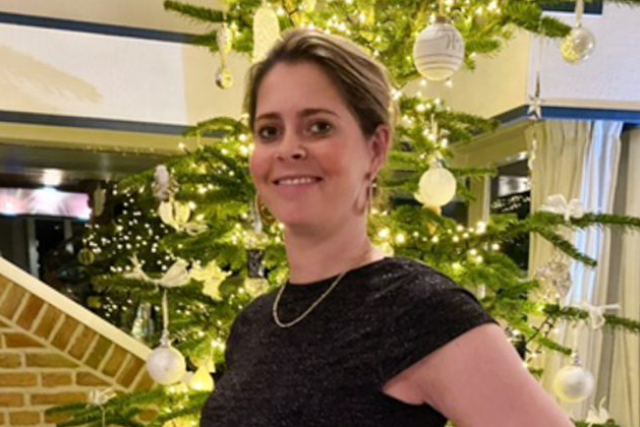Dr. Annalien Oosterbaan smiling in front of a decorated Christmas tree with white ornaments and warm lights, celebrating the holiday season indoors.