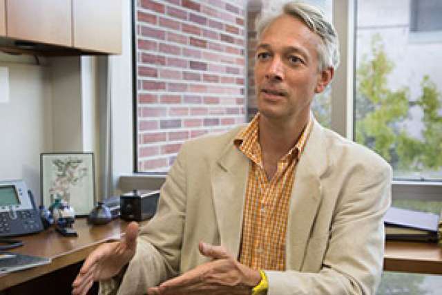 A person gesturing while seated at a desk in an office setting.