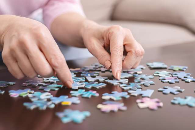 Senior woman playing jigsaw puzzle at home, close up