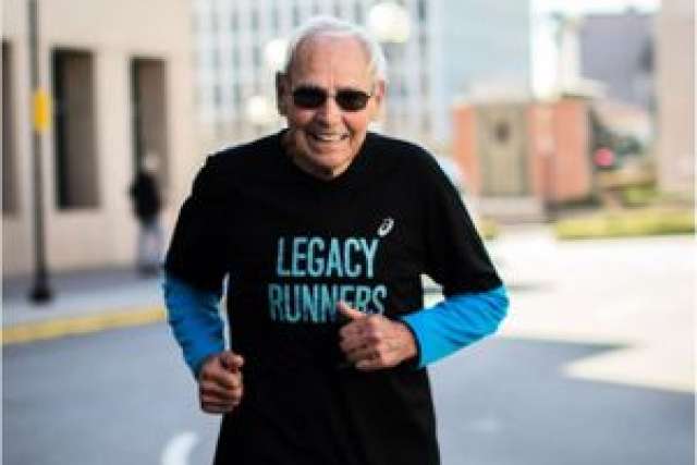 Person running in a "Legacy Runners" T-shirt, with a city backdrop.