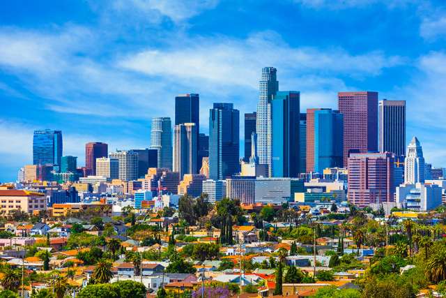 the Downtown Los Angeles skyline with several sky scapers and smaller buildings with green foliage