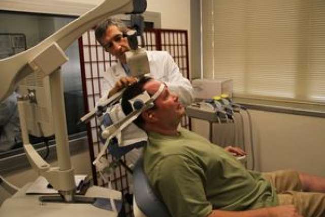 Dr. Andrew Leuchter adjusting equipment on a patient receiving treatment.