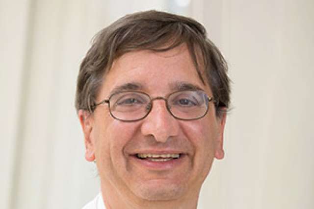 Dr. Jeffrey Saver, wearing a white coat and red-striped tie, smiles in front of a softly lit, light-colored background.