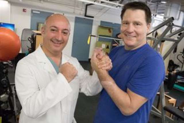Dr. Azari and Jonathan grip hands in a gym setting.