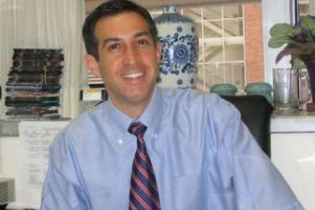 Dr. Gary Schiller in a light blue shirt and striped tie, seated at his desk.