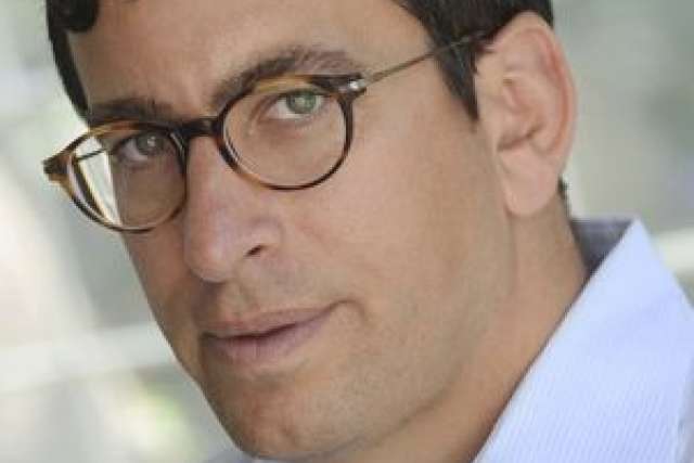 A man wearing a light blue shirt, blurred face, and short dark hair.