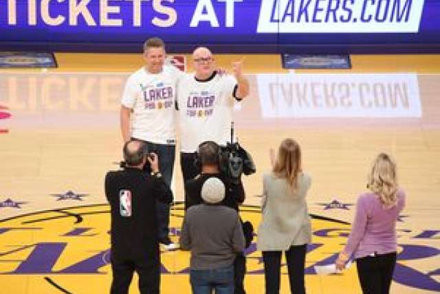 Two men in Lakers shirts celebrate on the court, surrounded by cameras and onlookers.