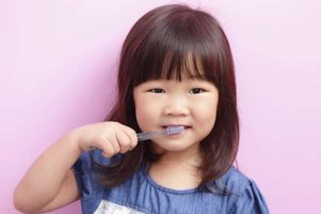Girl with toothbrush brushing her teeth against a pink background