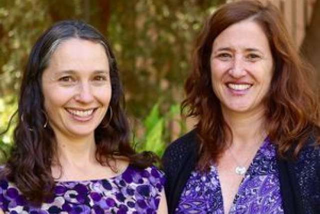 Two women with curly hair, wearing purple outfits, standing outdoors.