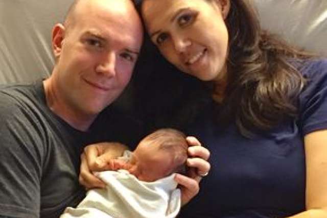 A couple holds their newborn baby, both smiling gently in a hospital setting.