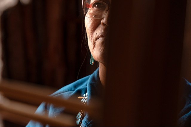 Navajo woman wearing glasses standing on a semi-dark room.