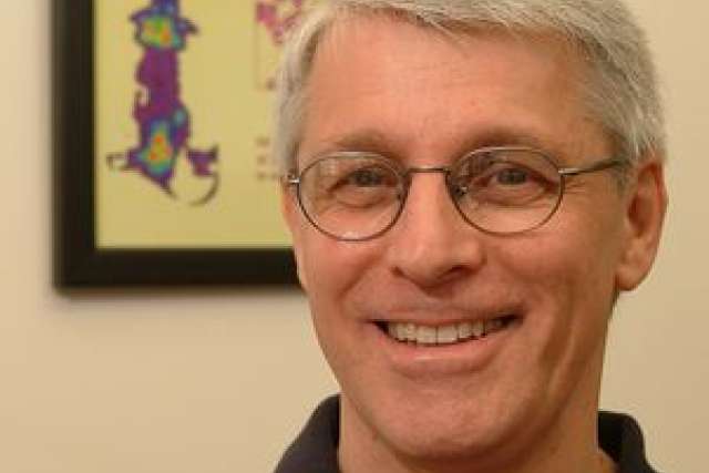 Researcher with gray hair in front of a colorful poster related to PET scans.
