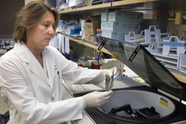 Scientist in a lab coat using a centrifuge in a laboratory setting.