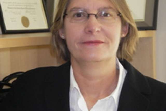 A person in a suit with framed diplomas in the background.
