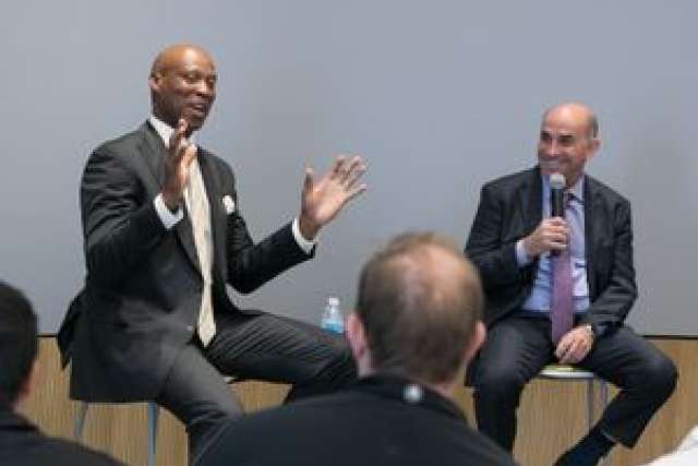 Two men in business attire engaged in conversation on stage.