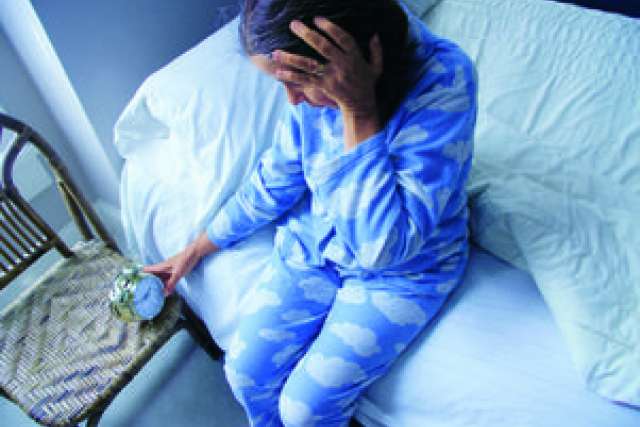 A woman in blue cloud-patterned pajamas sits on a bed, appearing distressed.