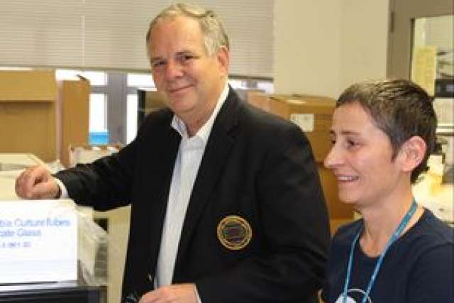 Two people standing by a table with boxes, one in a black blazer, another casually dressed.