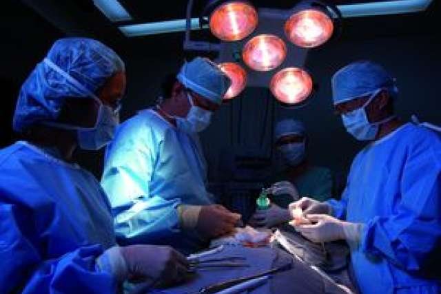A surgical team in blue scrubs performs a transplant surgery under bright lights.