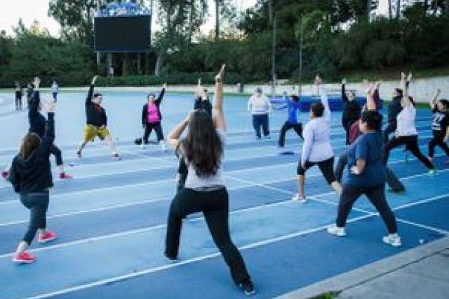 Participants in a group exercise class stretch on a sports track.