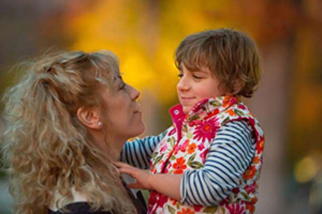 Woman holding a child outdoors during autumn, both smiling warmly.