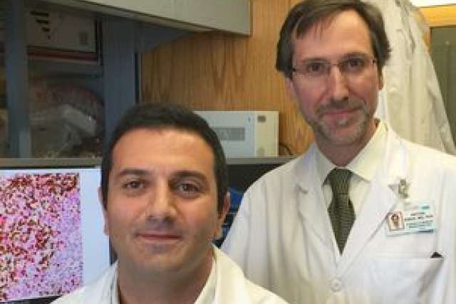 Two scientists in lab coats stand in a laboratory, with a microscope and images in the background.