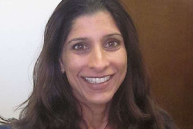 A woman with long dark hair seated indoors, wearing a gray sweater.