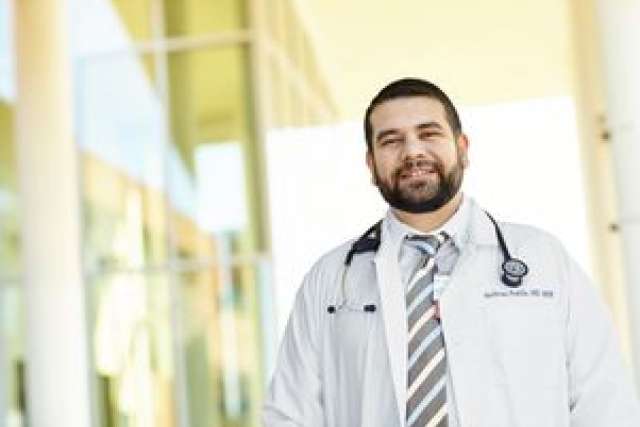 A physician wearing a white coat and stethoscope, standing outdoors.