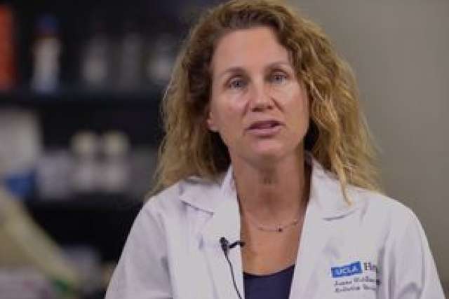 A person in a lab coat speaks in a laboratory setting.