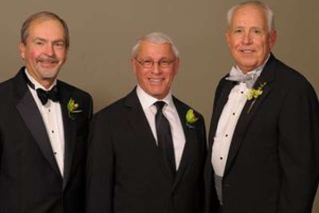 Three men in tuxedos with boutonnieres posing together.