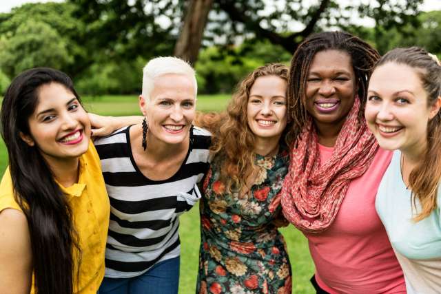 Five women standing and smiling in a park