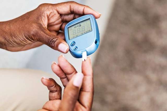 Close-up of hands using a blood glucose meter to check blood sugar, with a test strip inserted and finger ready for sampling.