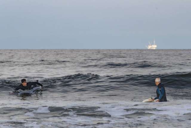 Dr. Sassoon and Robert Lombard swimming in the ocean on top of their surfboards. A white boat is visible in the background