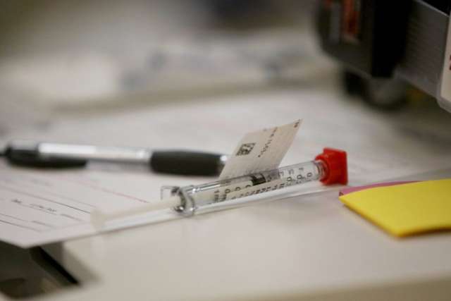 A close-up image of a pen and a vial containing the AstraZeneca Covid-19 vaccine sitting on a medical form on a table.