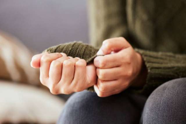 A person in a green sweater anxiously clasping their hands together.