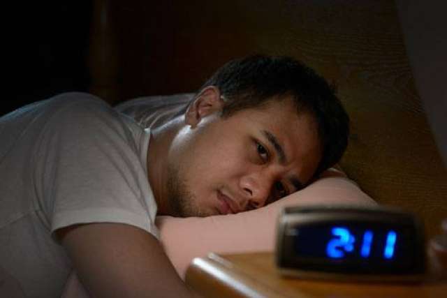 Man lying awake in bed watching alarm clock reading 2:11