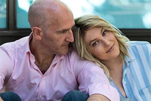 Two people sitting close together, one wearing a light pink shirt and the other in a blue striped shirt.