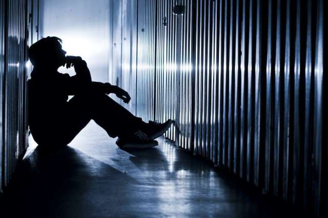 Backlit shadow of a man sitting on the floor in a hallway between jail cells