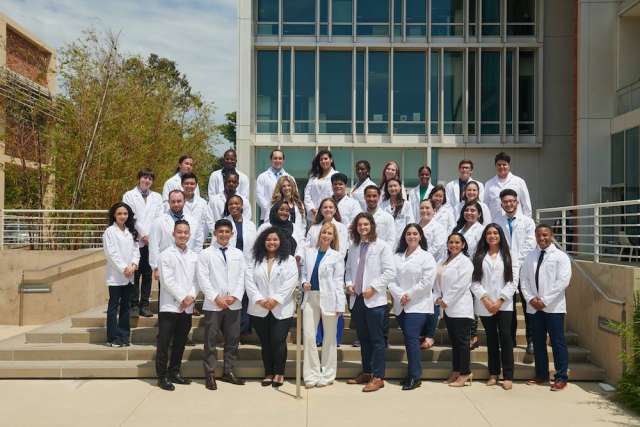UCLA PREP class of 2022 in white coats pose for a group photo on the steps outside of a modern building.