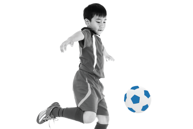 Black and white photo of a young boy in a soccer uniform jumping to kick a soccer ball