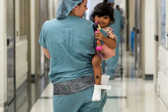 Nurse carrying a young girl down the hall