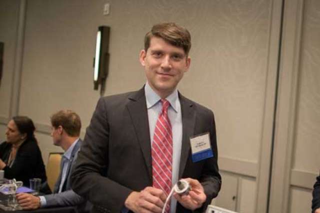 Dr Eugene DePasquale in suit holding a medical device with digital monitor.