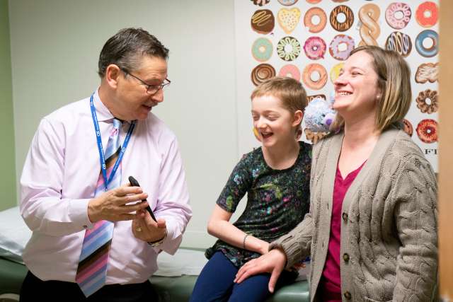 A doctor talks with a smiling child and a woman in a medical office.