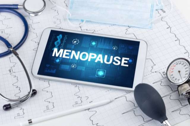 Tablet displaying the word 'Menopause' surrounded by medical tools including a stethoscope, blood pressure cuff, and face mask.