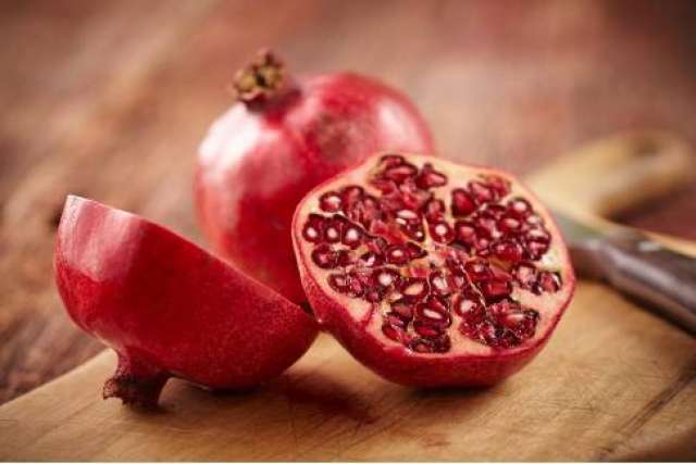 Fresh pomegranate cut open on a wooden surface, seeds visible inside.