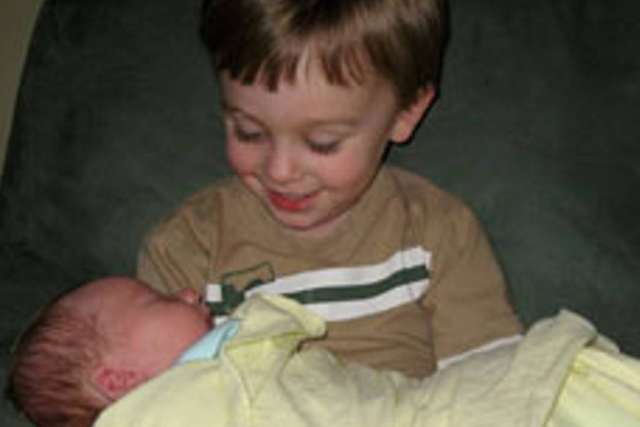 Smiling young boy holding a swaddled newborn.