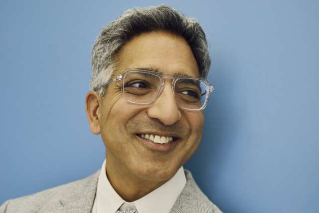 Smiling man in gray suit and patterned tie against a blue background
