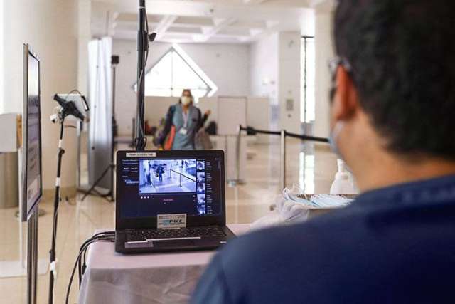 Person monitors a laptop showing live thermal scans of people entering a building for temperature screening.