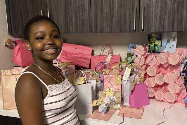Smiling girl beside table of pink gift bags and wrapped presents